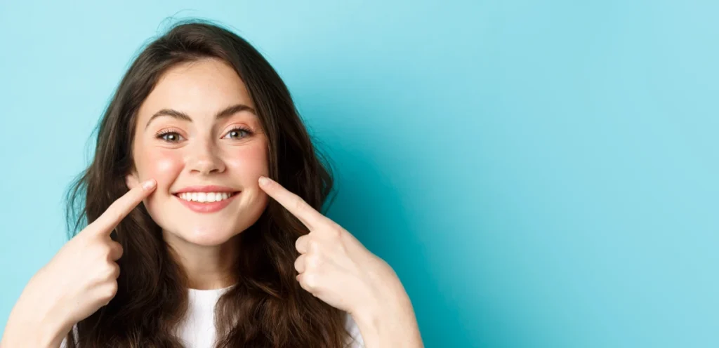 portrait happy young woman showing her clean glowing skin blush cheeks pointing fingers York House Dental Practice 2026 February